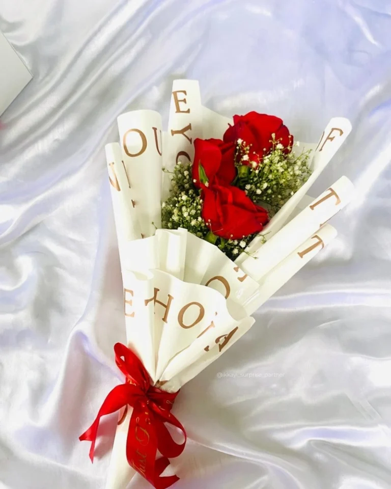 Three red rose bouquet wrapped in white 'LOVE' paper and a red ribbon.