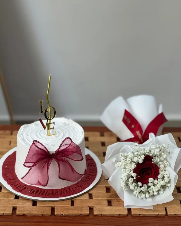 Small white birthday cake with pink flower bouquet and a white teddy bear gift set.