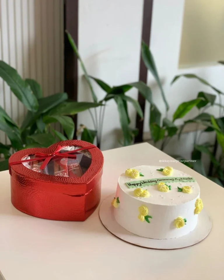 White cake with yellow roses, a heart-shaped velvet gift box, and a yellow rose bouquet.