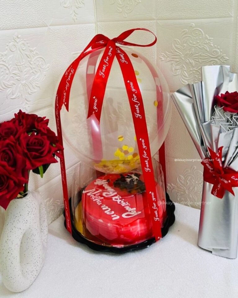 Red birthday cake inside a clear balloon gift bubble with a silver-wrapped rose.