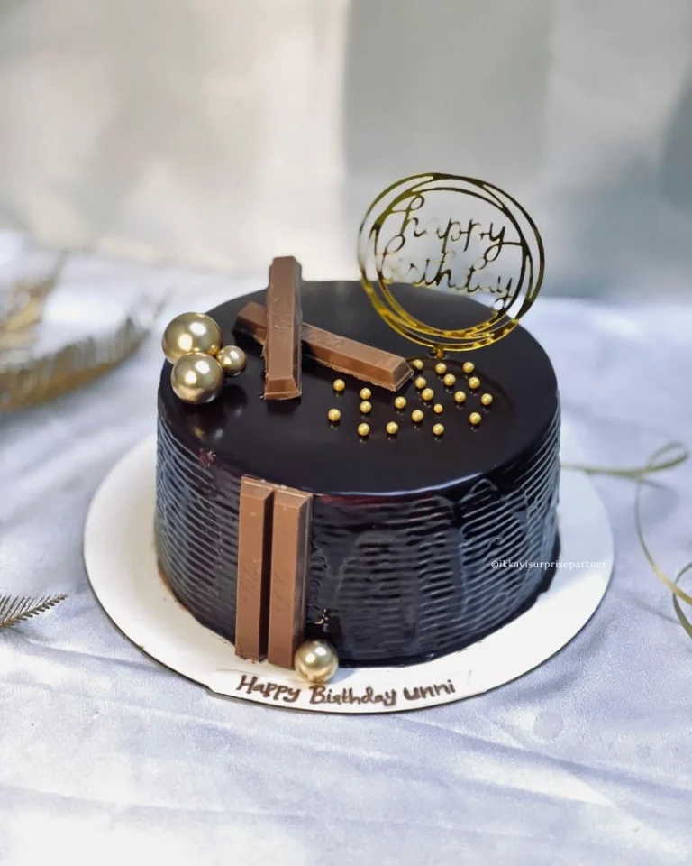 Glossy chocolate birthday cake with KitKat bars, gold spheres, and 'Happy Birthday' topper.