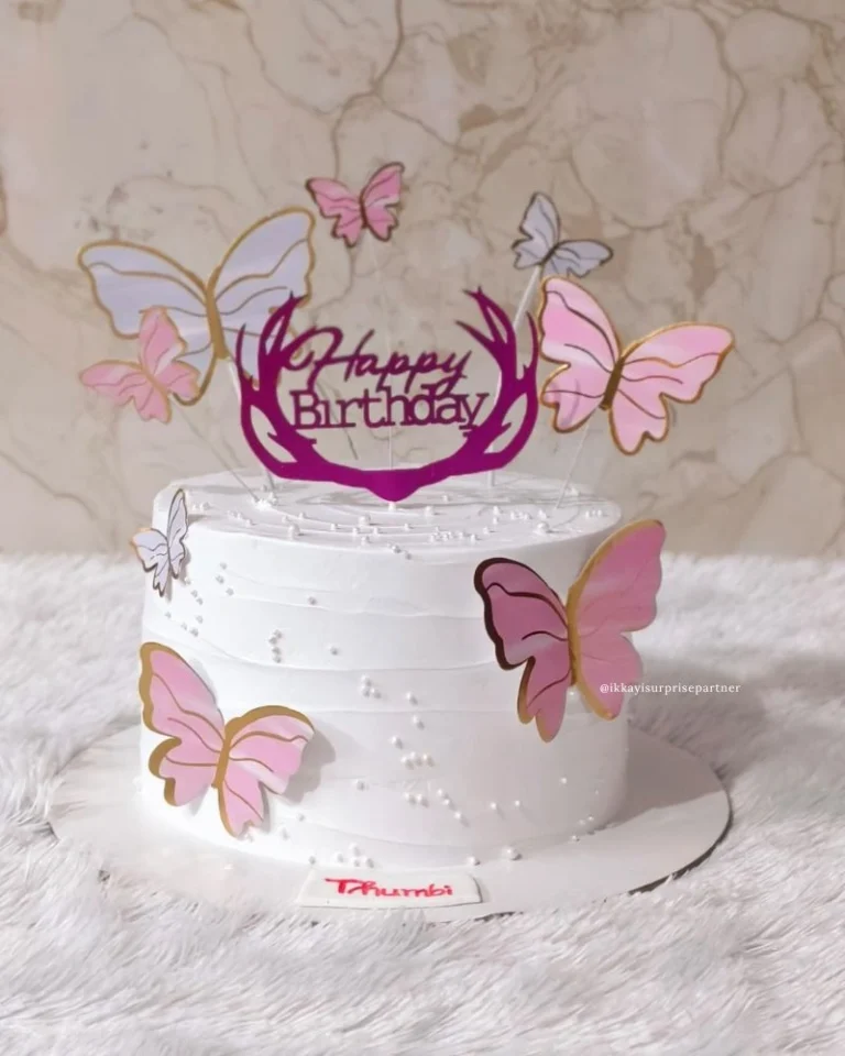 White birthday cake with pink butterfly cutouts and a 'Happy Birthday' topper.