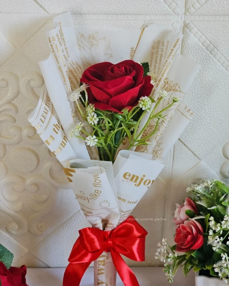 Single red rose bouquet with baby's breath and red ribbon, wrapped in gold-print paper.